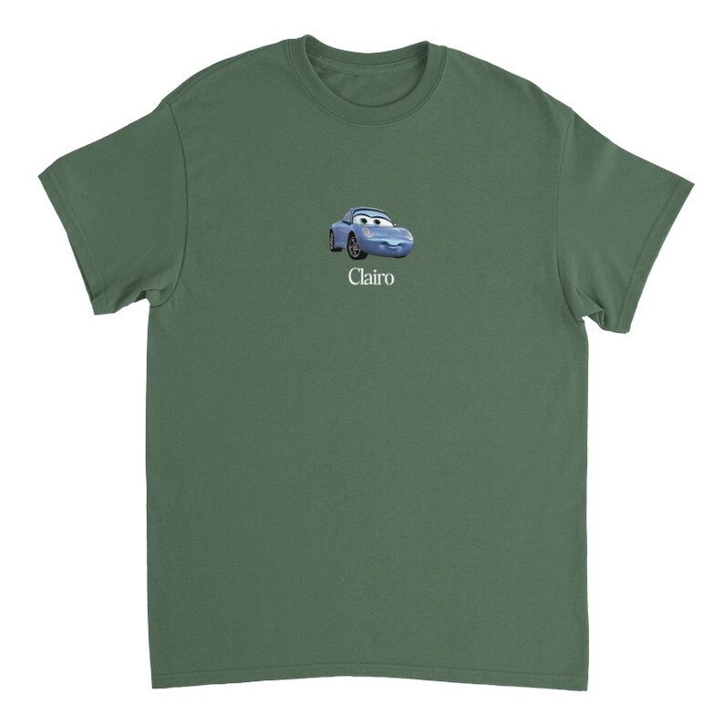 Op de afbeelding: Een groen T-shirt met korte mouwen met een blauwe cartoonauto en het woord "Clairo" erop gedrukt.
