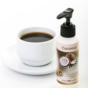 May include: A white bottle with a black pump top and a label that says "Coconut" with a picture of a coconut. The bottle is on a white surface next to a white cup of coffee.