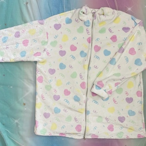 May include: White fleece zip-up jacket with a pastel pink, blue, yellow, and green heart and confetti pattern.