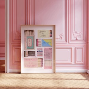 Puede incluir: Una obra de arte enmarcada con cajas de cerillas con varios textos, incluyendo "Enemies to Lovers" y "Fake Dating". La obra est&aacute; situada contra una pared rosa con molduras decorativas y un suelo de madera.