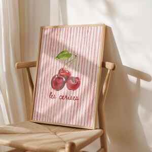 May include: A watercolour painting of red cherries on a pink and white striped background. The text "les cerises" is written in black below the cherries.