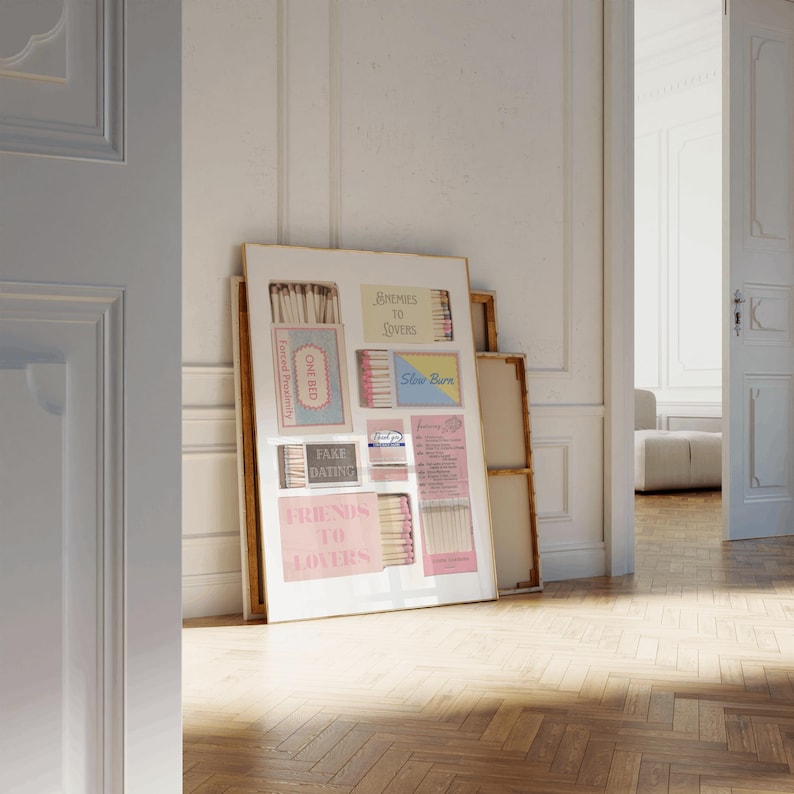 Puede incluir: Una obra de arte enmarcada con dise&ntilde;os de cajas de cerillas con textos como "Enemies to Lovers" y "Fake Dating". La obra se exhibe contra una pared blanca, con una vista de una habitaci&oacute;n a trav&eacute;s de una puerta abierta. El suelo es de madera.