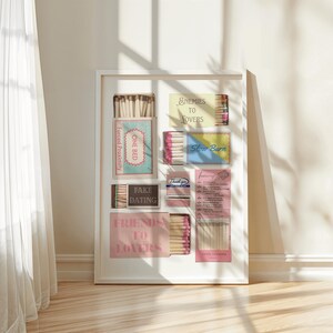Puede incluir: Una impresi&oacute;n art&iacute;stica enmarcada que presenta cajas de cerillas con textos como "Enemies to Lovers" y "Fake Dating". Las cajas de cerillas son de varios colores, incluyendo rosa, azul y amarillo, sobre un fondo blanco.