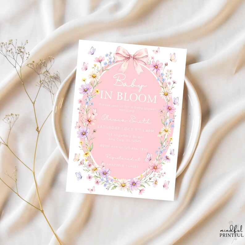 May include: A baby shower invitation with the text "Baby in Bloom" in a pink oval, surrounded by a floral wreath and butterflies. The invitation includes the name Olivia Smith, date, time, and address.