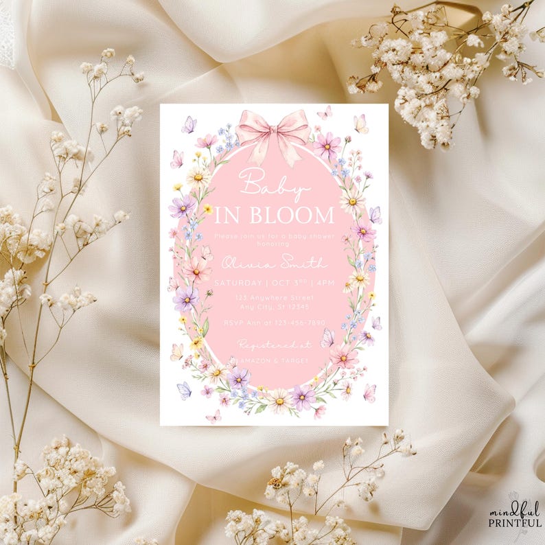 May include: A baby shower invitation with the text "Baby in Bloom" in a pink oval, surrounded by a floral border with butterflies. The invitation includes event details and is set against a cream-colored fabric.