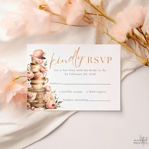 May include: A white RSVP card with gold script that reads "kindly RSVP" for a tea party. The card features a stack of teacups and pink floral accents. The text includes the date February 20, 2026.