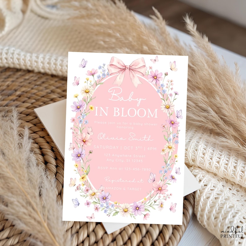 May include: A baby shower invitation with the text "Baby in Bloom" in a pink oval surrounded by flowers and butterflies. The invitation includes details such as the date, time, and RSVP information.