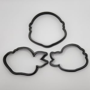 May include: Three black plastic cookie cutters, one shaped like a head, one shaped like a fish, and one shaped like a cloud.