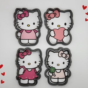 Puede incluir: Cuatro cortadores de galletas con forma de Hello Kitty. Cada cortador presenta un diseño diferente: uno con un lazo, otro con un corazón, uno con una flor y otro con un lazo y un corazón.