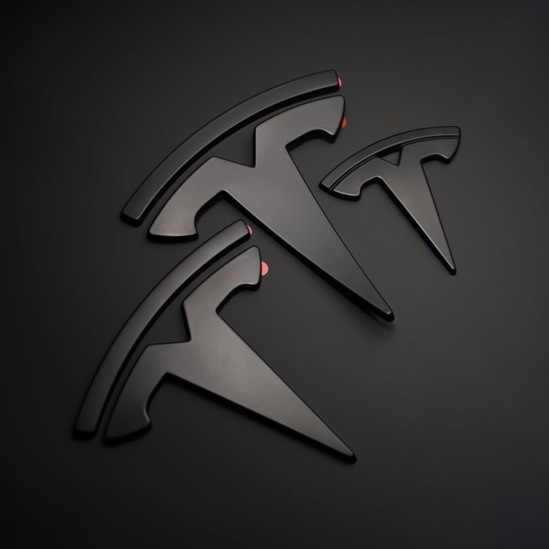 May include: Three black metal Tesla logos of different sizes, arranged in a triangular pattern on a black background.