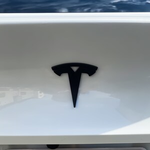 May include: A black Tesla logo on a white car.