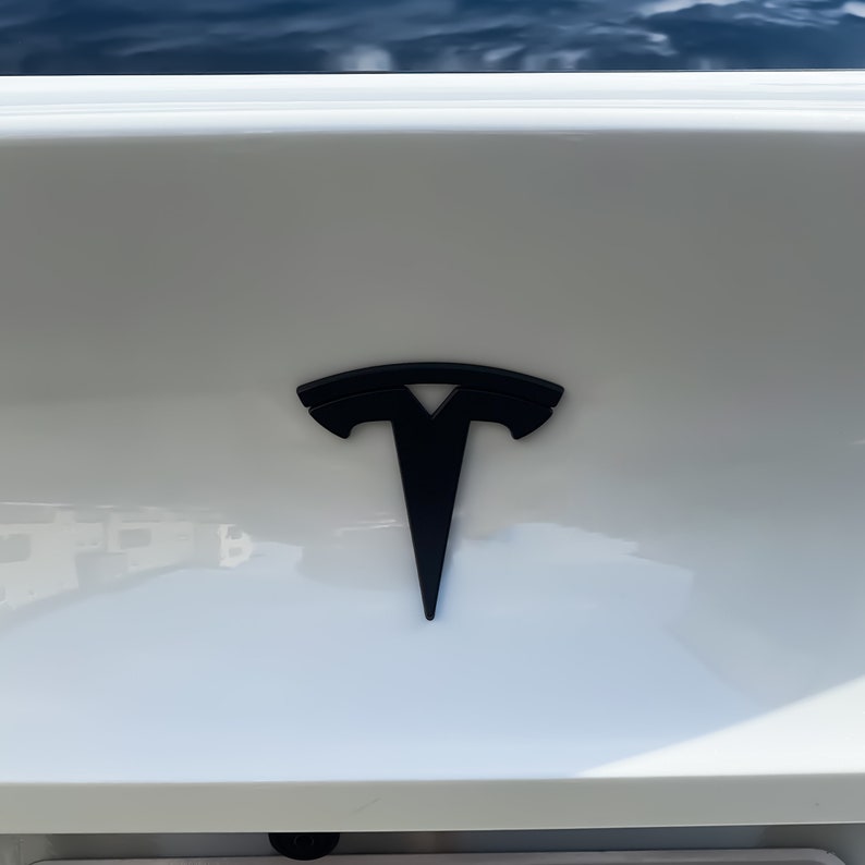 May include: A black Tesla logo on a white car.