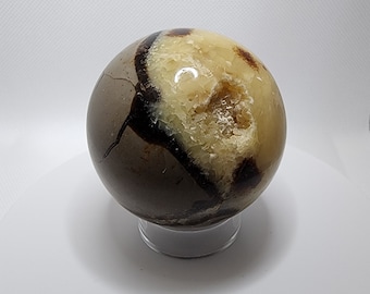 May include: A polished sphere of geode with brown and white banding. The geode has a large opening revealing a crystal-lined interior.