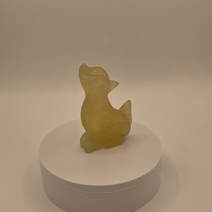 May include: A small, yellow, carved figurine of a wolf, sitting on a white pedestal.