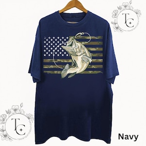 May include: Navy blue t-shirt featuring a graphic of a fish jumping out of the water, with a fishing hook and line. The design incorporates the American flag with a camouflage pattern. The word "Navy" is printed at the bottom right.