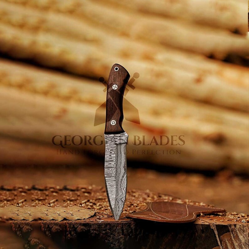 May include: A handcrafted, Damascus steel knife with a dark wood handle. The knife is sharp and has a distinctive pattern on the blade. The text "GEORG BLADES HAND FORGED TO PERFECTION" is visible on the image.
