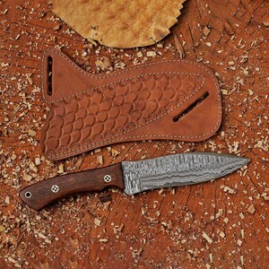 May include: A brown leather sheath with a decorative pattern and a  damascus steel knife with a wooden handle.
