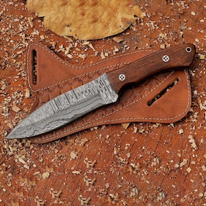 May include: A brown leather sheath with a decorative pattern holds a knife with a Damascus steel blade and a dark wood handle.