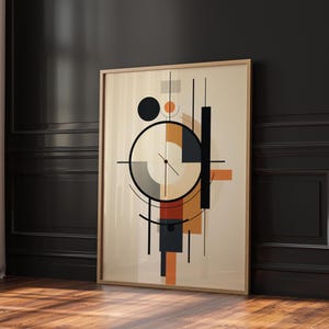 May include: Abstract geometric art print in a wooden frame. The artwork features a beige background with black, orange, and gray shapes, including circles, lines, and rectangles. The framed art is leaning against a dark wall on a wooden floor.