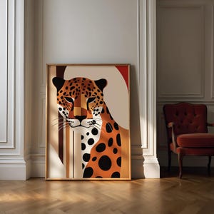 Puede incluir: Lámina artística enmarcada con una ilustración estilizada de un leopardo. La obra de arte muestra la cara y la parte superior del cuerpo del leopardo con colores naranja, negro y crema. La impresión está en un marco de madera y se exhibe en una habitación con una silla roja.