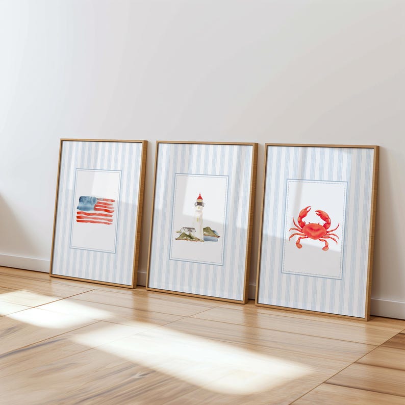 May include: Three framed watercolor prints with nautical themes. The prints feature an American flag, a lighthouse, and a red crab. Each print has a white border and is set against a blue and white striped background.