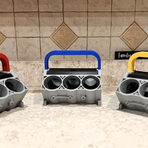 May include: Three 3D printed can holders shaped like a car engine block. Each holder has a different colored handle: red, blue, and yellow.