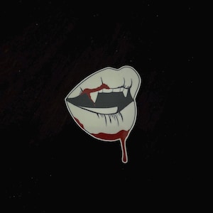 May include: A white and red illustration of a vampire's mouth with fangs and dripping blood.