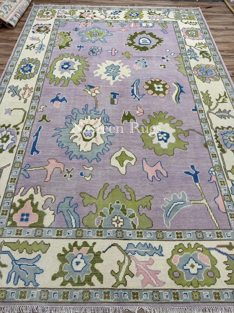 May include: A rectangular rug with a lavender central field and a cream border. The rug displays floral and geometric patterns in green, blue, and pink. The text "Green Rugs" is visible on the rug.