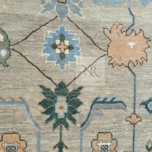 K&ouml;nnte beinhalten: Ein beiger Teppich mit einem sich wiederholenden Muster aus blauen, gr&uuml;nen und braunen floralen Motiven. Der Teppich hat einen dezenten Used-Look.