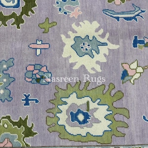 May include: Close-up of a lavender rug with a floral pattern. The design features white, green, blue, and pink floral motifs. The text "Nasreen Rugs" is visible on the rug.
