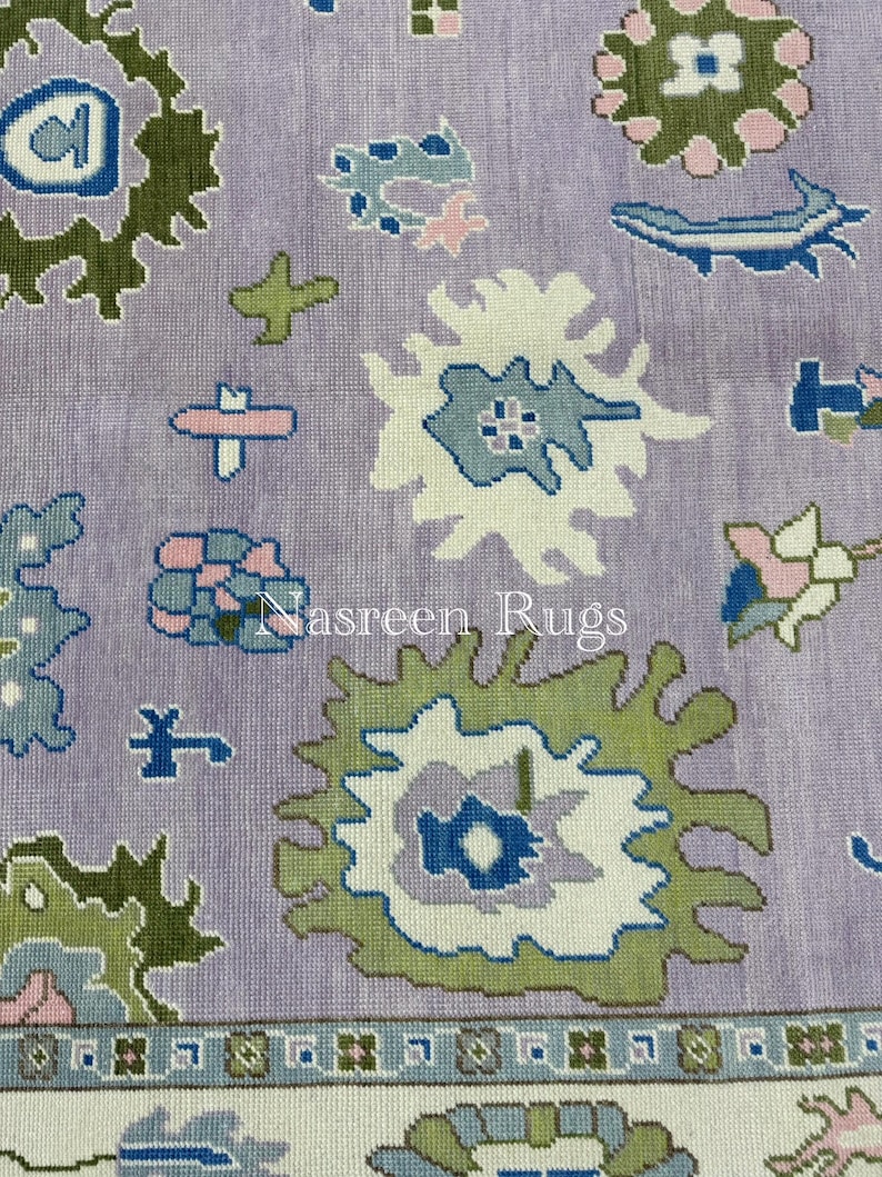 May include: Close-up of a lavender rug with a floral pattern. The design features white, green, blue, and pink floral motifs. The text "Nasreen Rugs" is visible on the rug.