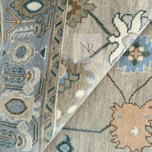 K&ouml;nnte beinhalten: Nahaufnahme eines hellblauen und beigen gemusterten Teppichs mit aufwendigen Blumendesigns. Der Teppich hat einen dezenten Glanz und eine weiche Textur.