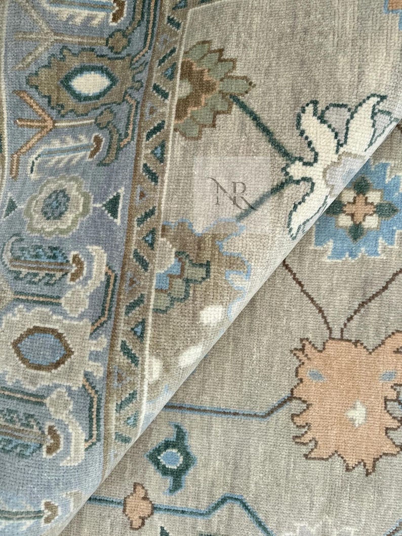 K&ouml;nnte beinhalten: Nahaufnahme eines hellblauen und beigen gemusterten Teppichs mit aufwendigen Blumendesigns. Der Teppich hat einen dezenten Glanz und eine weiche Textur.