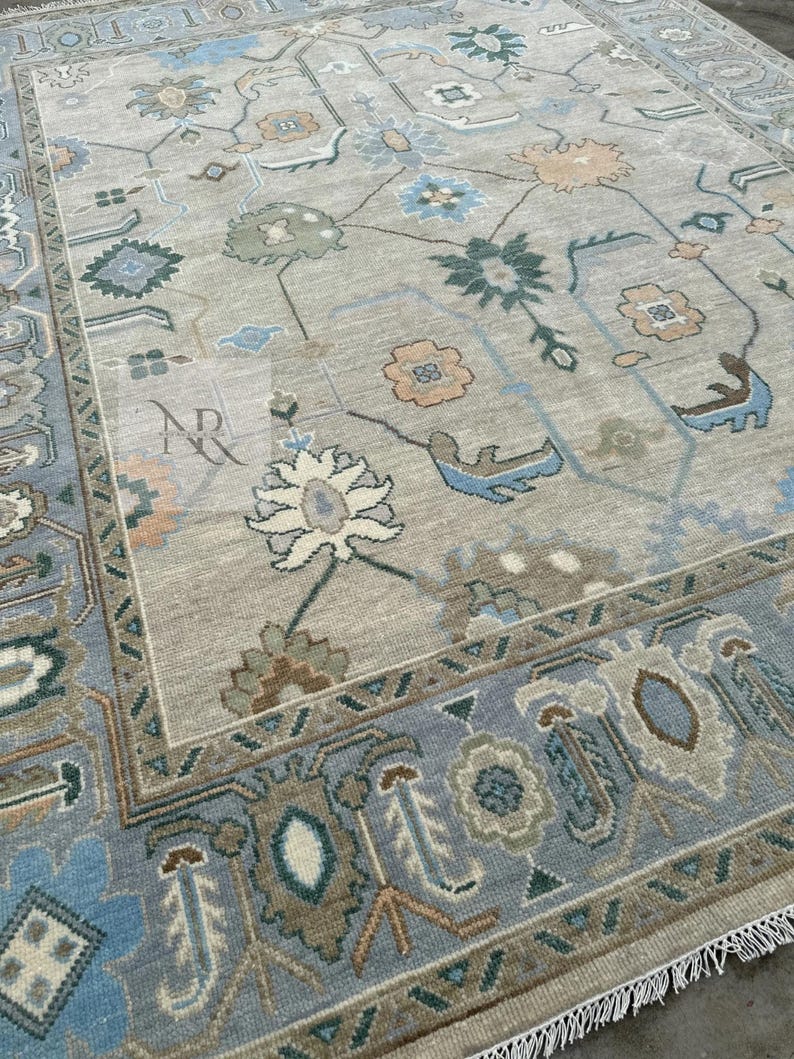 K&ouml;nnte beinhalten: Ein hellblauer und beiger Teppich mit einem Blumenmuster. Der Teppich hat einen Fransenrand und ist aus Wolle.