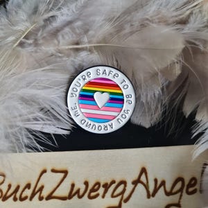Könnte beinhalten: Weißer Emaille-Pin mit einem Regenbogen und einem weißen Herzen in der Mitte. Der Text um den Pin herum lautet "You're safe to be around me".