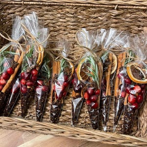 以下が含まれることがあります： 紐で結ばれた透明なセロハン袋がいくつか入った、編まれたバスケット。各バッグには、シナモンスティック、乾燥オレンジスライス、クランベリー、八角、ローズマリーの小枝など、さまざまな材料が混合されており、お祝いの雰囲気を醸し出しています。