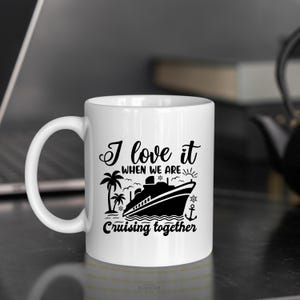 May include: White ceramic coffee mug with a black graphic of a cruise ship and palm trees. The text reads "I love it when we are cruising together".