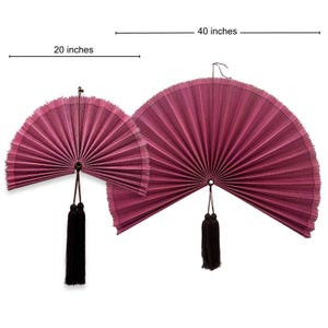 May include: Two semi-circular wall fans in a deep magenta color with pleated textures. The smaller fan measures 20 inches and the larger fan measures 40 inches. Each fan features a dark brown hanging tassel attached to the center pivot point.