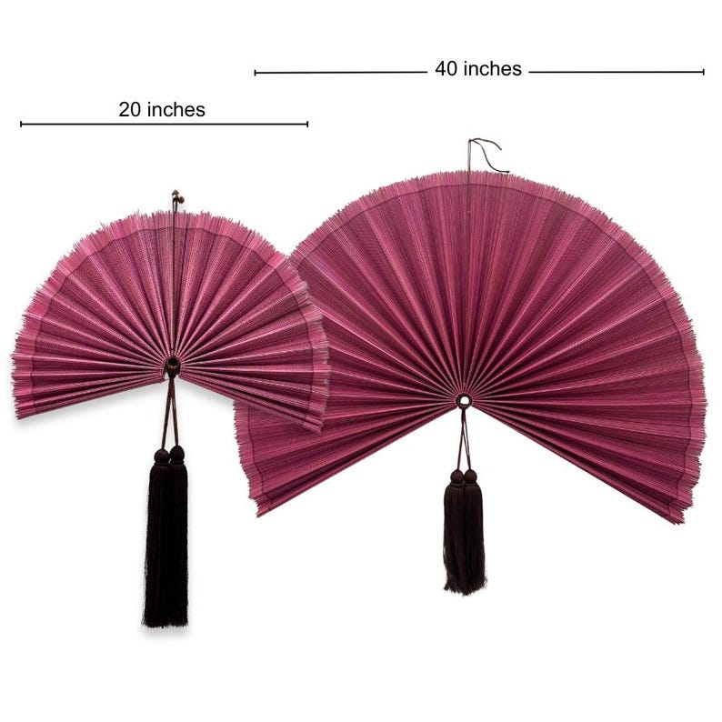 May include: Two semi-circular wall fans in a deep magenta color with pleated textures. The smaller fan measures 20 inches and the larger fan measures 40 inches. Each fan features a dark brown hanging tassel attached to the center pivot point.