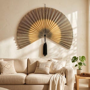 May include: A large, semi-circular wall fan featuring a gradient design that transitions from a dark, textured outer edge to a lighter, golden-yellow center. The fan is constructed with fine, radiating pleats and includes a black tassel hanging.