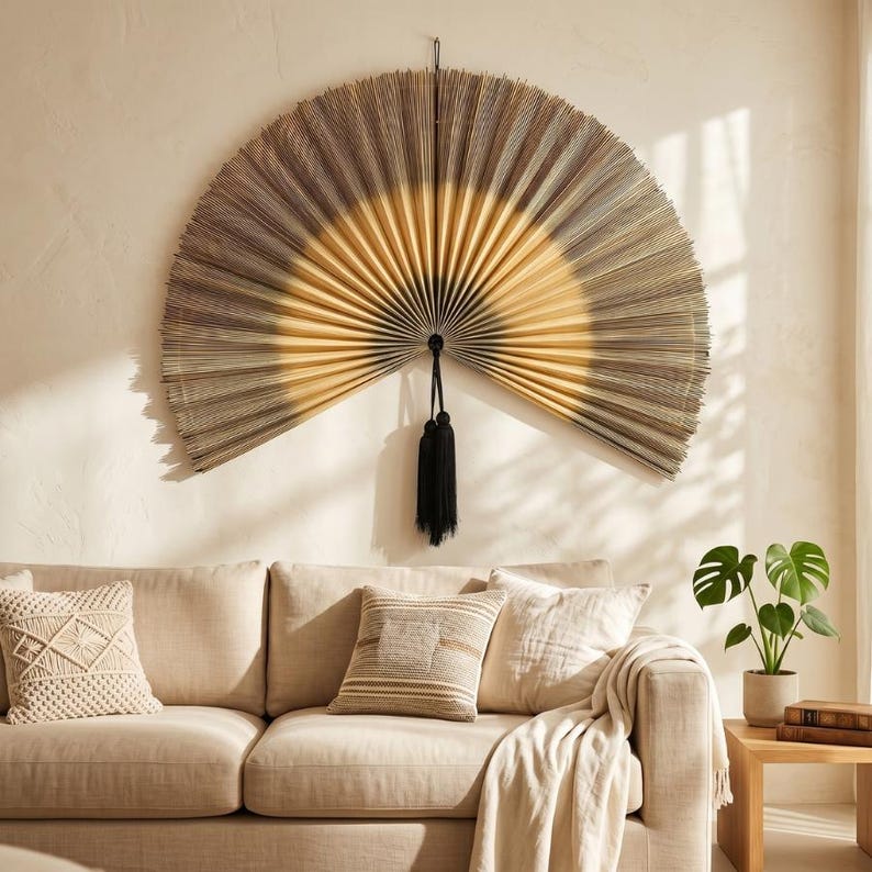 May include: A large, semi-circular wall fan featuring a gradient design that transitions from a dark, textured outer edge to a lighter, golden-yellow center. The fan is constructed with fine, radiating pleats and includes a black tassel hanging.