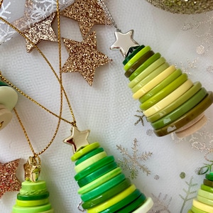 May include: A set of four green and yellow button Christmas tree decorations with silver star toppers. The decorations are hanging from gold cords.