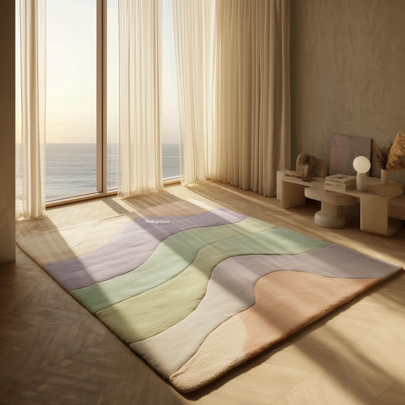 May include: A large, rectangular area rug with a wavy, color-blocked design. The rug features pastel shades of lavender, green, peach, and cream. The rug is placed on a wooden floor in a room with large windows and sheer curtains.
