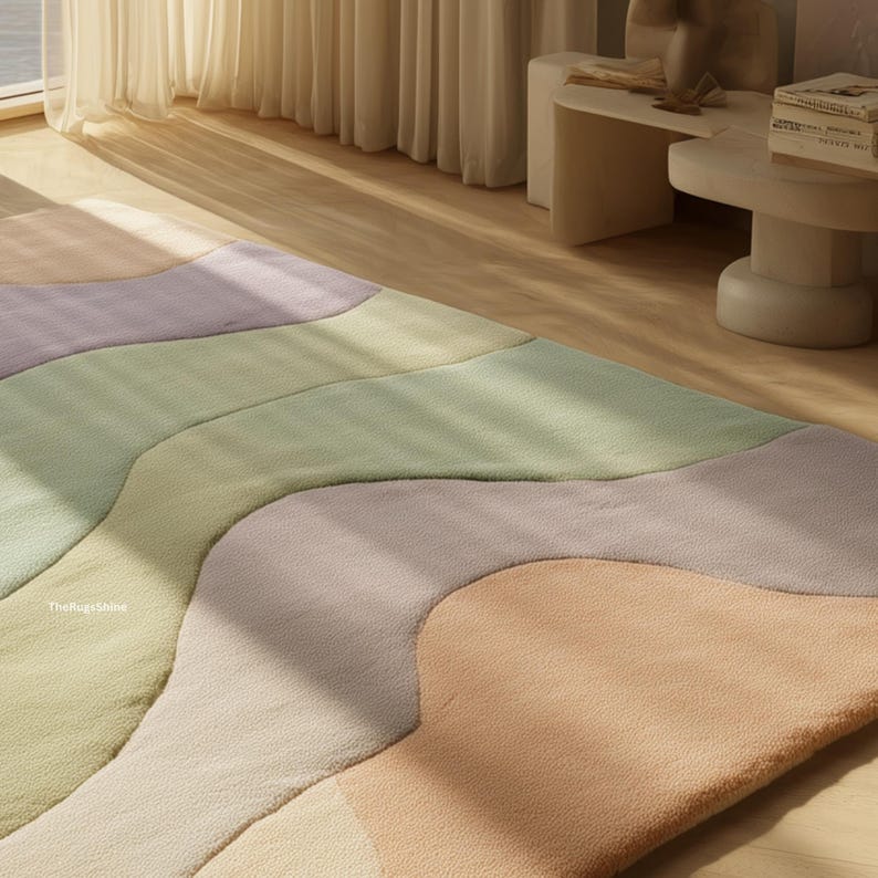 May include: A colorful area rug with an abstract design. The rug features soft pastel colors including peach, lavender, green, and cream. The rug is made of a plush material and is placed on a hardwood floor.