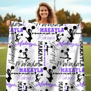 Könnte beinhalten: Weiße Fleece-Decke mit einem sich wiederholenden Muster aus einer Cheerleader-Silhouette, lila Sternen und dem Namen "Makayla" in einer lila und schwarzen Schriftart.