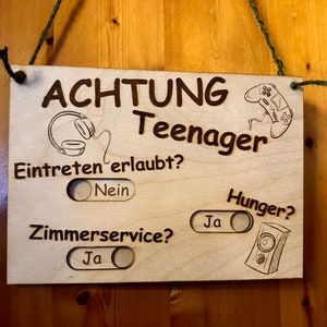 Könnte beinhalten: Ein Holzschild mit dem Text "ACHTUNG Teenager" und einem Kippschalter, der "Eintreten erlaubt?" mit den Optionen "Nein" und "Ja" lautet. Es gibt einen weiteren Kippschalter, der "Hunger?" mit den Optionen "Nein" und "Ja" lautet. Das Schild hat auch einen Kippschalter, der "Zimmerservice?" mit den Optionen "Nein" und "Ja" lautet.