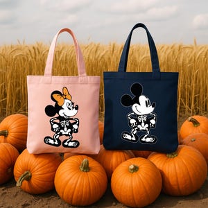 May include: Two tote bags, one pink and one navy blue, each featuring a cartoon skeleton character. The pink bag has a Minnie Mouse design with an orange bow. The navy bag has a Mickey Mouse design. The bags are surrounded by orange pumpkins.