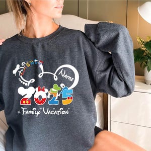 a woman sitting on a bed wearing a mickey mouse sweatshirt