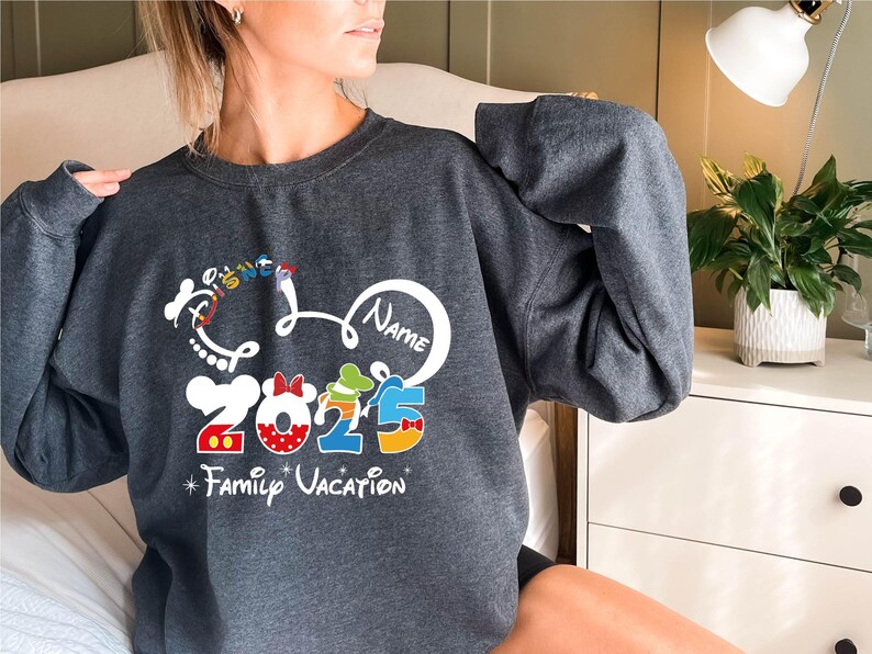 a woman sitting on a bed wearing a mickey mouse sweatshirt