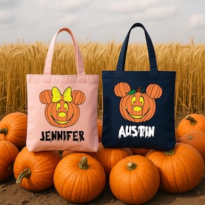 Puede incluir: Dos bolsas de mano de Halloween, una rosa y otra azul marino, cada una con un diseño de calabaza sonriente con orejas de ratón. La bolsa rosa tiene el nombre "Jennifer" y la bolsa azul tiene el nombre "Austin" impresos. Las bolsas están rodeadas de calabazas naranjas.